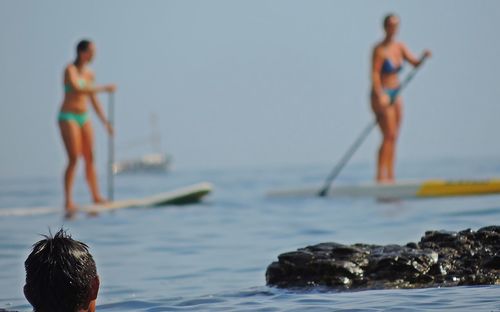 Rear view of man looking at women in biking paddleboarding on sea