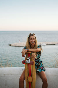 Laughing female with long board skate in front of mediterranean sea