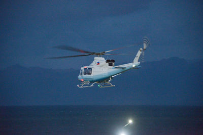 Helicopter flying over sea against blue sky