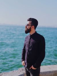 Handsome man standing at beach against sky