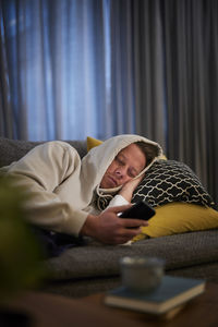 Ill man lying on sofa with smartphone