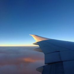 Low angle view of airplane wing against clear blue sky