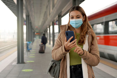 Traveler woman wearing mask at train station buying ticket online with her mobile phone outdoor