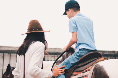 Boy sitting on horse with man standing by and looking away