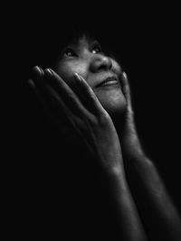 Close-up of smiling thoughtful woman against black background