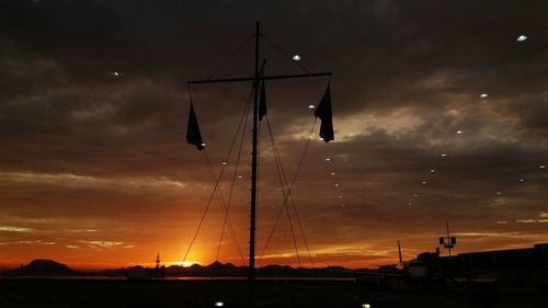 Low angle view of silhouette cranes against dramatic sky during sunset