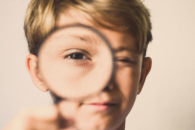 Close-up portrait of boy holding magnifying glass against wall