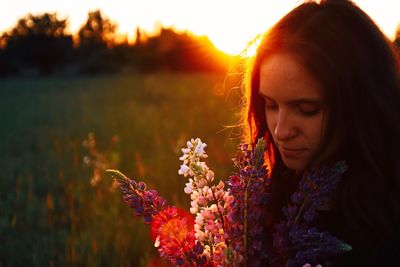 Portrait of woman with pink flowers on field during sunset