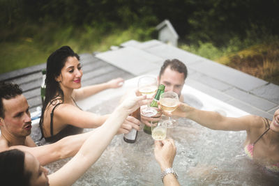 Carefree male and female friends toasting drinks in hot tub during weekend getaway