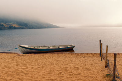 Foggy morning landscape scenery with old wooden fishing boat on sandy beach of loch na fooey 