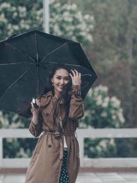 Portrait of young woman with umbrella standing in rain