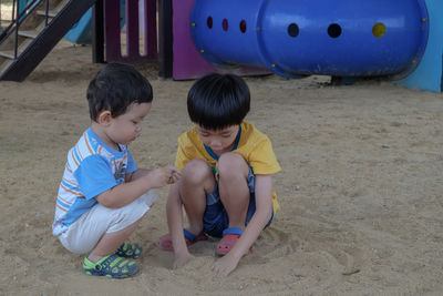 Full length of cute boys playing with sand at playground