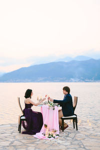 Rear view of couple sitting on mountain against sky