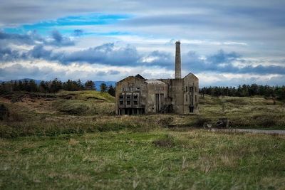 Abandoned house on grassy field against cloudy sky