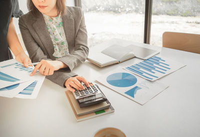 Midsection of woman using smart phone while sitting on table