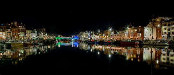Weymouth harbour scene at night with reflections in still water.