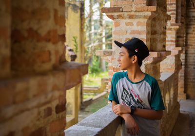 Man looking away while standing against brick wall