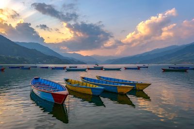 Boats moored in sea against sky during sunset