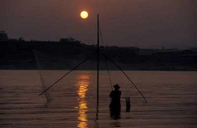 Silhouette man fishing in lake against sky during sunset