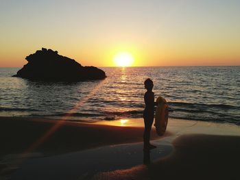 Silhouette boy holding inflatable ring while standing on shore at beach against sky during sunset