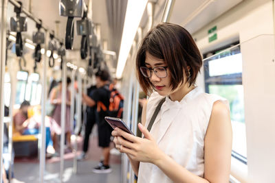 Asian young short hair woman wearing glasses using and looking her smartphone in train