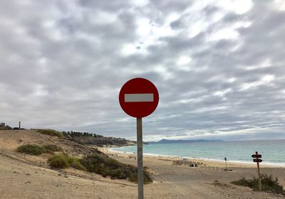 Road sign on beach against sky