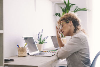 Side view of young woman using laptop at home