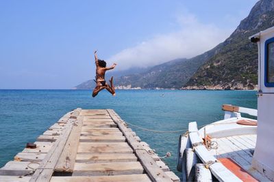 Woman jumping on pier over sea against sky