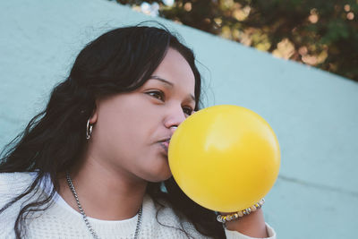 Close-up of woman blowing yellow balloon