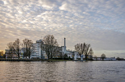 Buildings by river against sky during sunset