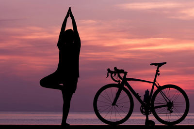 Silhouette bicycle by sea against sky during sunset