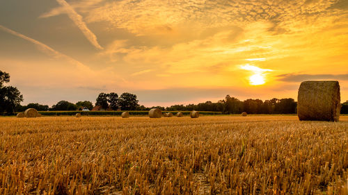 Hay bales on field against sky during sunset