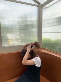 Low section of woman using mobile phone by window