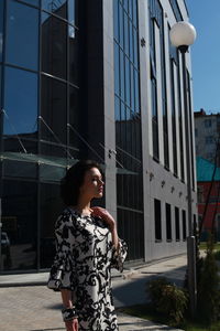 Fashionable young woman wearing floral patterned dress standing against building in city