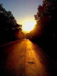 Road amidst trees against clear sky during sunset