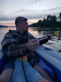 Midsection of man sitting on boat against sky during sunset