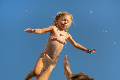 Baby girl flying in against blue sky.father throwing kid up