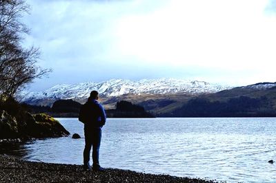 Rear view of man looking at lake against mountain