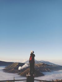 Young woman looking away while standing on railing against sky