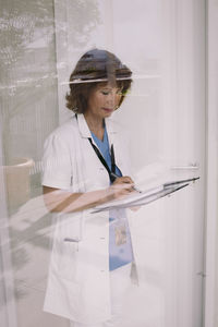 Senior female physician examining medical record seen through glass