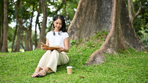 Young woman using mobile phone while sitting on tree trunk