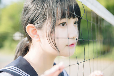 Close-up of thoughtful young woman looking away by net outdoors