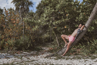 Side view of woman on tree trunk amidst plants