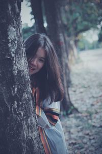 Portrait of woman standing by tree trunk in forest