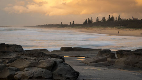 Rocks on shore against sky during sunset