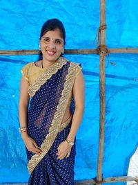 Portrait of young woman standing against blue tarpaulin