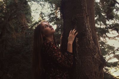 Young woman looking at tree trunk in forest