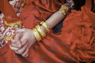 Midsection of woman in red sari wearing gold bangles