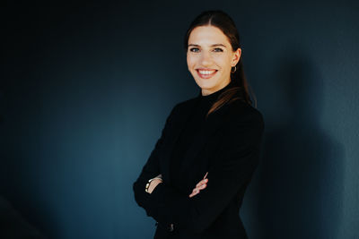 Portrait of a smiling young woman standing against wall