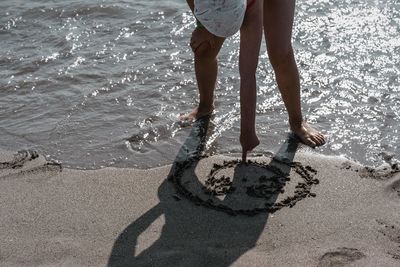 Woman drawing on sand against sea at beach